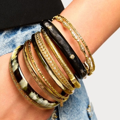 Conjunto de braceletes dourados e pretos no pulso com jeans e roupa preta