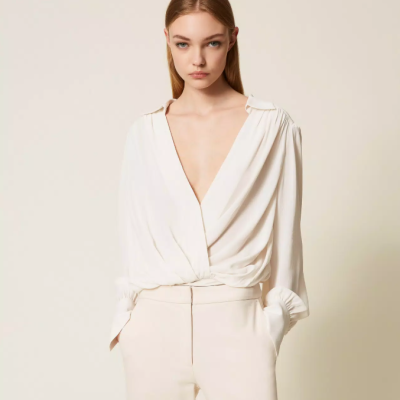 Mulher com blusa branca de tecido leve e decote em V profundo, e calças claras de cintura subida