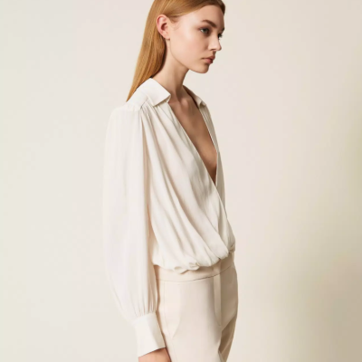 Blusa branca fluida de manga comprida com decote em V profundo e franzido na cintura, usada por mulher com calças claras.
