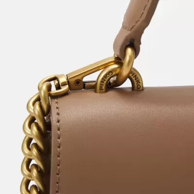 Detalhe de bolsa bege em pele com alça corrente dourada e gravação PINKO