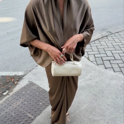 Pessoa com vestido castanho e mala branca numa rua