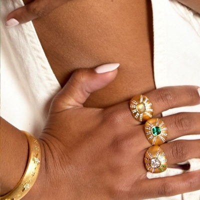 Mãos femininas com vários anéis e bracelete dourado em fundo claro