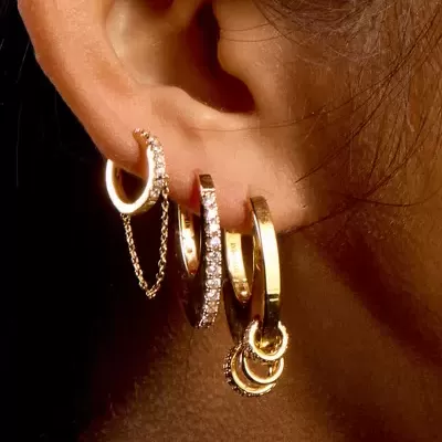 Brincos de argola dourados com pedras e corrente mostrados na orelha de uma mulher