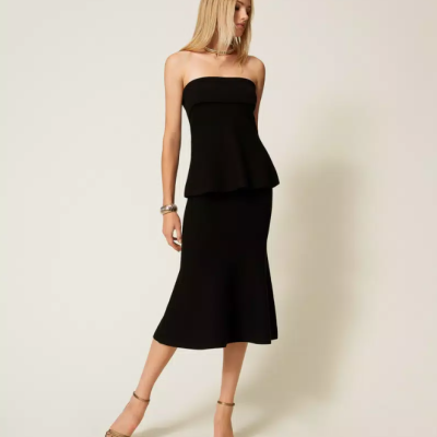 Conjunto feminino preto com top sem alças e saia midi em fundo neutro.