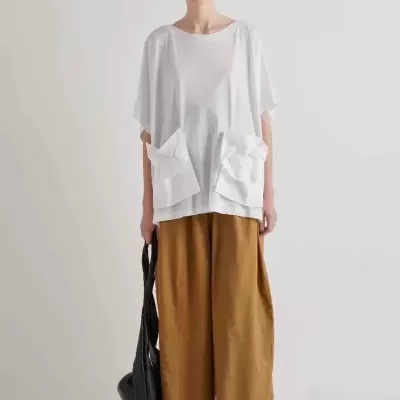 Modelo com t-shirt branca solta com bolsos, calças largas camel, sapatilhas brancas e mala preta