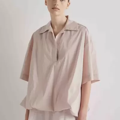 Mulher com camisa oversize rosa pálido e saia clara em fundo branco