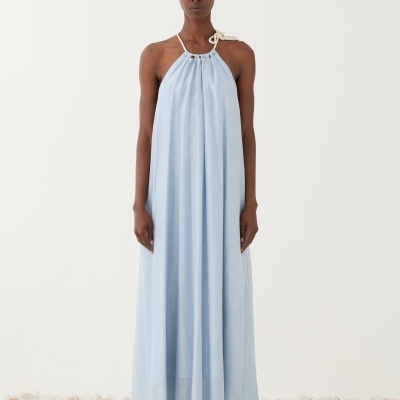 Vestido longo azul claro com decote halter e sandálias, modelo em pé sobre pedras.