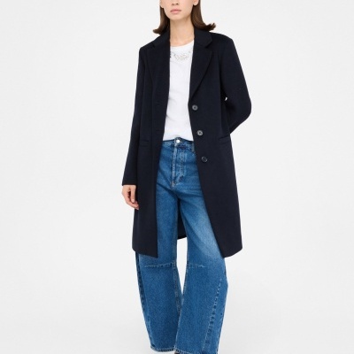 Mulher com casaco preto, jeans azul largo e sapatos pretos em fundo branco