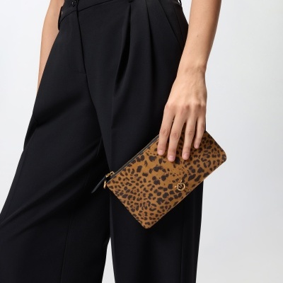 Carteira padrão animal print castanho preto com fecho dourado, mão segurando, calças pretas
