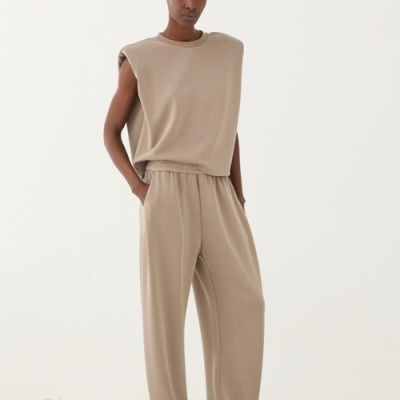 Conjunto bege feminino com colete sem mangas e calças largas, calçado branco em chão de pedras brancas