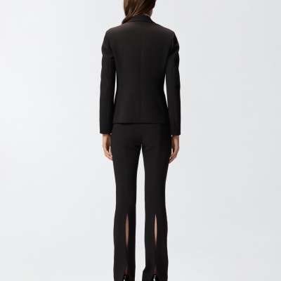 Fato feminino preto visto de costas com blazer e calças justas com aberturas