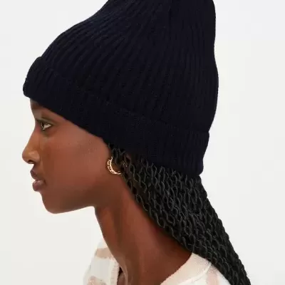 Mulher de perfil a usar gorro preto de malha com dobra e camisola riscada bege e branca