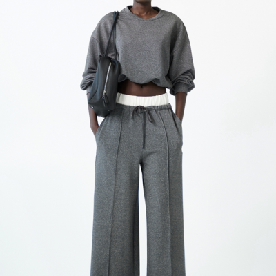 Mulher com conjunto cinza de sweatshirt e calças largas, bolsa preta e óculos escuros.