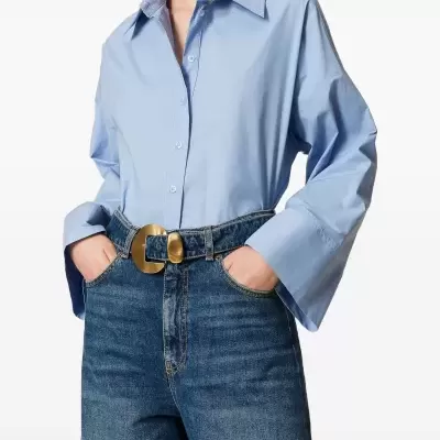 Camisa azul clara de algodão com botões e mangas largas, jeans azul escuro e cinto com fivela dourada