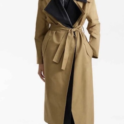 Mulher com casaco longo bege e detalhes em preto, botas pretas e óculos de sol