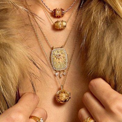Colares e anéis dourados com pedras brilhantes usados numa pessoa com casaco de pêlo