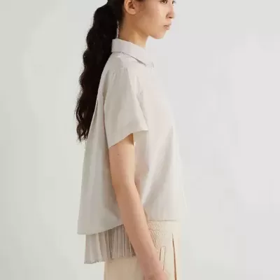 mulher de perfil com camisa cremosa de manga curta e saia bege