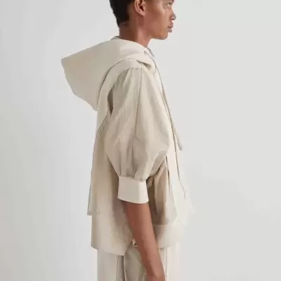 Pessoa com roupa bege clara de mangas bufantes e capuz