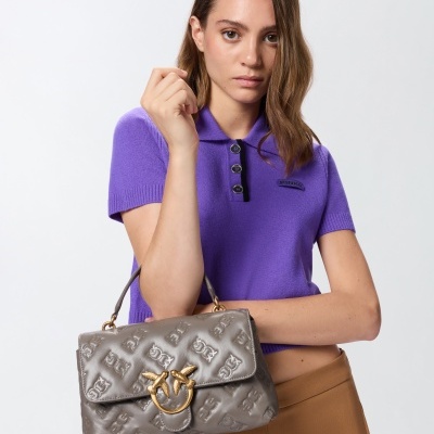 Mulher com camisa roxa, calças castanhas e mala cinza com padrão em relevo e fecho dourado