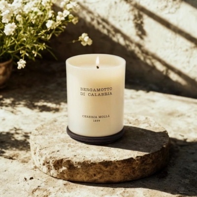 Vela aromática branca BERGAMOTTO DI CALABRIA sobre base de pedra com flores ao fundo