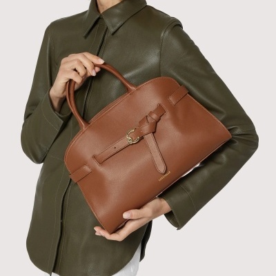 Mala castanha de couro com fivela dourada nas mãos de mulher com camisa verde escuro