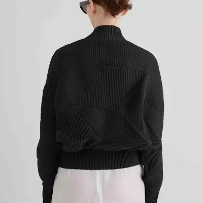 Pessoa de costas com casaco preto de padrão geométrico e saia branca translúcida.