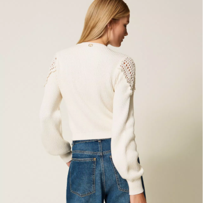 Casaco branco de malha com detalhes rendados nos ombros e calças jeans azuis