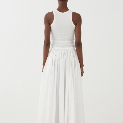 Pessoa de costas com top branco canelado e saia longa branca sobre seixos.