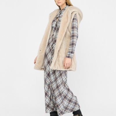 Mulher com casaco de pelo sintético bege, vestido xadrez comprido e botas pretas com tachas