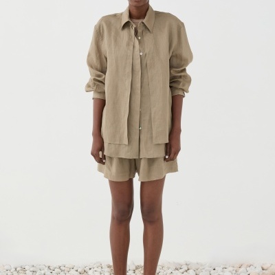 Mulher com conjunto bege de camisa e calções de linho e sandálias castanhas em cenário com pedras brancas no chão.