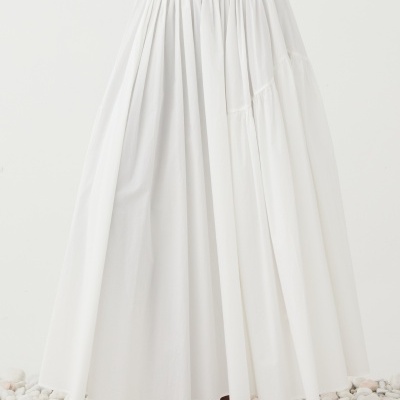 Saia comprida branca com cintura elástica e sandálias bege em chão de pedras brancas