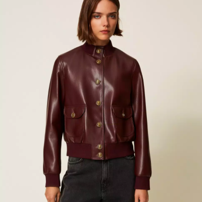 Casaco bomber vinho em pele sintética com botões dourados e bolsos, punhos em malha, usado com calças pretas.