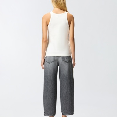 Modelo de costas com camisola branca sem mangas, calças cinza de ganga largas e sapatos prateados.