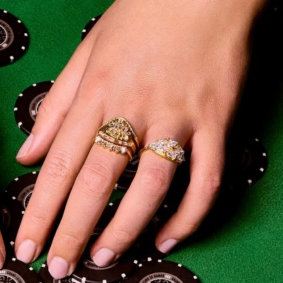 Anéis dourados com pedras em mão sobre mesa de jogo verde com fichas de poker pretas.