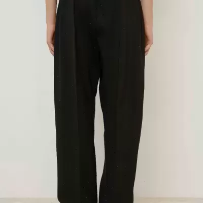 Calças negras largas com cintura e tornozelos elásticos em fundo neutro