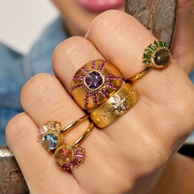 Mão com cinco anéis de metal dourado e pedras coloridas