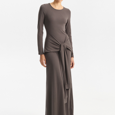 Modelo com vestido castanho comprido e nó na cintura, botins pretos e óculos de sol escuros