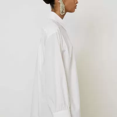 Mulher com camisa branca, saia castanha e brincos grandes em fundo branco