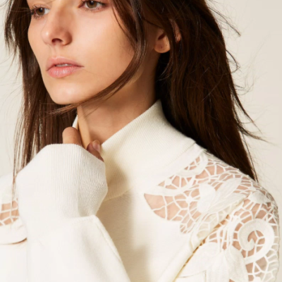 Mulher com camisola branca de gola alta e detalhes em renda floral nas ombreiras