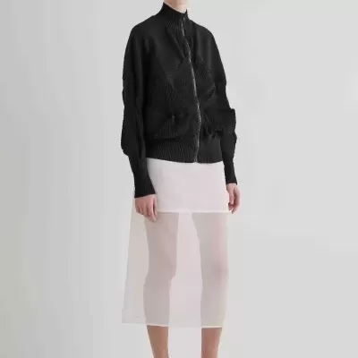 Casaco preto textura padrão, saia branca transparente, sapatos brancos salto médio, óculos escuros, fundo cinza