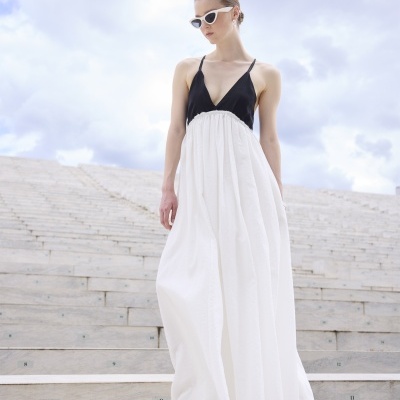 Mulher com vestido longo preto e branco e sandálias brancas em escadaria de pedra ao ar livre