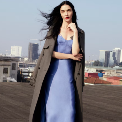 Mulher a usar vestido azul claro e casaco cinza em ambiente urbano