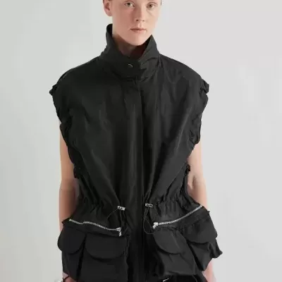 Colete preto sem mangas com bolsos frontais e gola alta em fundo neutro.