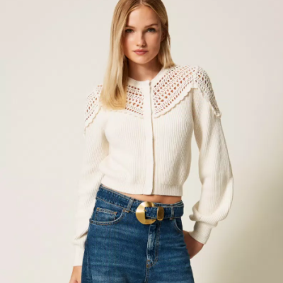 Mulher com casaco branco de malha e calças de ganga azuis num fundo branco