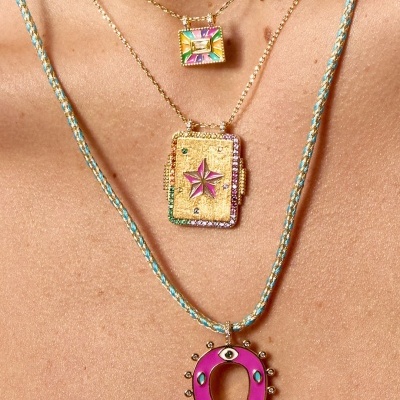 Três colares femininos com pendentes coloridos e dourados usados no pescoço.