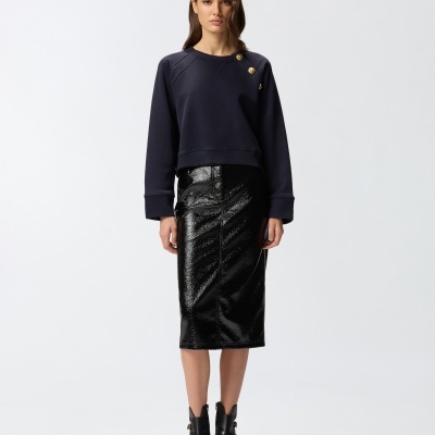 Modelo feminina com sweatshirt azul escuro, saia lápis preta brilhante e botas negras com fivelas.