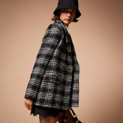 Mulher com casaco às riscas preto e branco, chapéu preto e mala preta em fundo castanho.