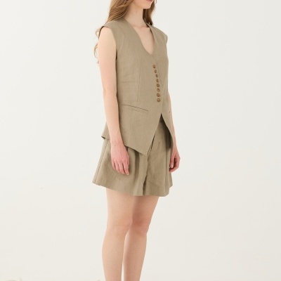 mulher com colete bege sem mangas, calções bege largos e sandálias riscas azuis e brancas sobre pedras