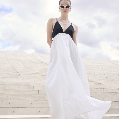 Vestido longo preto e branco com sandálias brancas, óculos de sol e escadaria de mármore numerada.