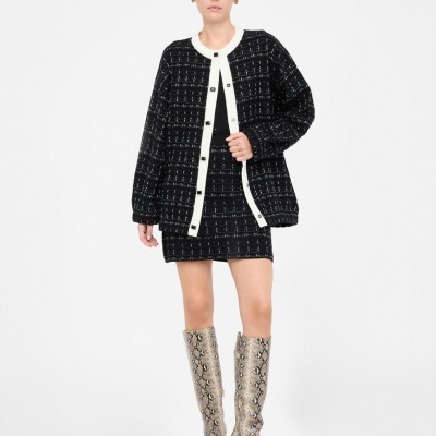 Mulher com casaco e saia pretos de padrão com linhas brancas e botas altas com padrão de pele de cobra